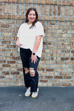 Load image into Gallery viewer, Woman wearing a white t-shirt and black ripped jeans standing against a brick wall.