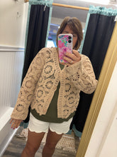 Load image into Gallery viewer, woman wearing a beige lace cardigan over a green top and white shorts, taking a mirror selfie.
