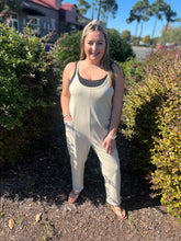 Load image into Gallery viewer, Woman in a beige jumpsuit standing outdoors among bushes