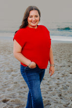 Load image into Gallery viewer, Woman in a red sweater and blue jeans standing on a beach.