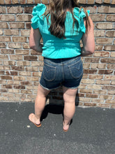 Load image into Gallery viewer, Person wearing a turquoise top and denim shorts standing against a brick wall.