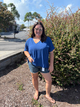 Load image into Gallery viewer, Woman in a blue shirt standing outdoors next to a bush