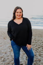 Load image into Gallery viewer, Woman standing on a beach wearing a black long sleeve ribbed top and blue jeans.
