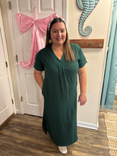 Load image into Gallery viewer, Woman in a green dress standing in a room with a pink robe on a chair.