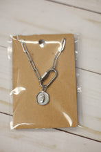 Load image into Gallery viewer, Silver carabiner necklace with a charm on a brown card with clear plastic wrap, on a tiled floor.