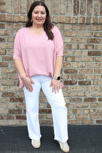 Load image into Gallery viewer, Woman wearing a pink top and white pants standing against a brick wall