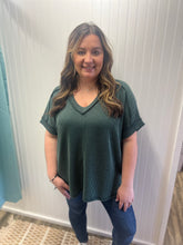 Load image into Gallery viewer, Woman wearing a green textured top and blue jeans in a fitting room.