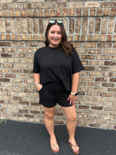 Load image into Gallery viewer, Woman wearing a black outfit standing against a brick wall.