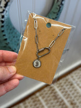 Load image into Gallery viewer, Small chain necklace with a pendant on a brown card held by a hand.