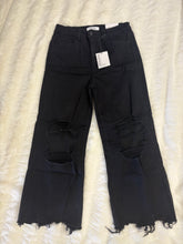 Load image into Gallery viewer, Black distressed jeans with a tag on a white textured surface