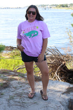 Load image into Gallery viewer, Person wearing a purple shirt with a crocodile graphic in front of a water fountain