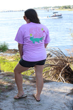 Load image into Gallery viewer, Person wearing a purple t-shirt with a graphic design, standing near a waterfall.
