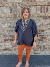 Load image into Gallery viewer, Woman wearing a black and leopard top and rust pants standing against a brick wall.
