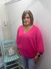 Load image into Gallery viewer, Woman in a pink shirt standing indoors with a light blue chair and decorative pillow in the background.