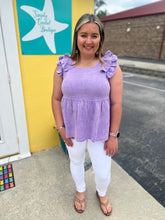 Load image into Gallery viewer, Woman wearing a purple top with ruffled sleeves and white pants standing in front of a store entrance.