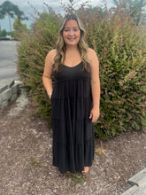 Load image into Gallery viewer, Woman wearing a black dress standing outdoors with greenery in the background