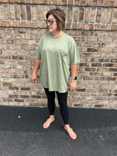 Load image into Gallery viewer, Woman wearing a green t-shirt and black leggings standing against a brick wall.