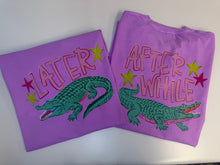 Load image into Gallery viewer, Two folded purple t-shirts with alligator graphics and text on a white background