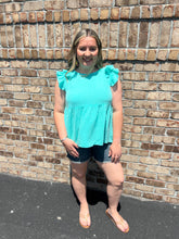Load image into Gallery viewer, Woman wearing a mint top and denim shorts standing against a brick wall.