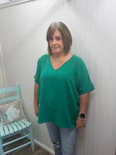 Load image into Gallery viewer, woman wearing a green top and light colored jeans standing indoors against a white wall