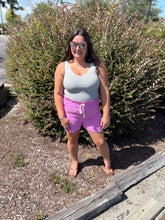 Load image into Gallery viewer, Woman wearing a light gray tank top and pink shorts standing outdoors near bushes.