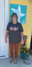 Load image into Gallery viewer, Woman standing in front of a store with a sign in the background wearing a charcoal thankful tshirt with rust pants