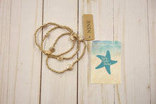 Load image into Gallery viewer, set of 3 Gold bracelet on a wooden surface with a card featuring a shell design.