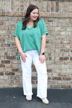 Load image into Gallery viewer, Woman wearing a green top and white pants standing against a brick wall