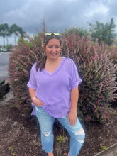 Load image into Gallery viewer, Woman wearing a purple shirt and ripped jeans standing in front of bushes on a cloudy day.
