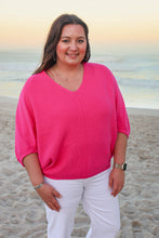 Load image into Gallery viewer, Woman in a bright pink sweater and white pants standing on a beach.
