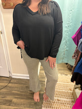 Load image into Gallery viewer, Woman wearing a black long sleeve top and lt olive pants standing in a room with a light blue wall.