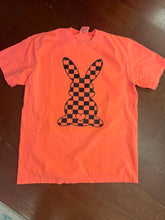 Load image into Gallery viewer, Neon Coral t-shirt with a black checkered bunny design on a wooden surface