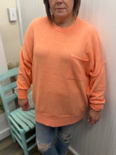 Load image into Gallery viewer, Person wearing an orange sweatshirt standing in a room with a light blue chair and white wall.