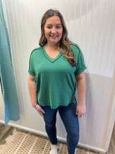 Load image into Gallery viewer, Woman wearing a green ribbed top and blue jeans standing in front of a white wall.