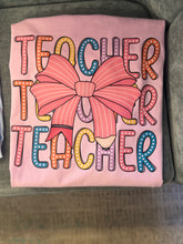 Load image into Gallery viewer, Pink stacked Teacher tee laying on a couch