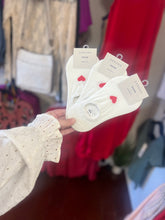 Load image into Gallery viewer, Hand holding white socks with red hearts and brand tags against a blurred background
