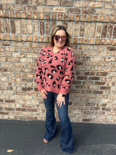 Load image into Gallery viewer, Woman wearing a pink leopard print sweater and blue jeans standing against a brick wall.
