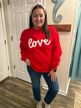 Load image into Gallery viewer, Person wearing a red sweatshirt with 'LOVE' printed on it, standing indoors.
