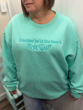 Load image into Gallery viewer, Person wearing a mint sweatshirt with 'I'd rather be at the beach' text and shell graphics.
