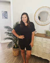 Load image into Gallery viewer, A woman wearing a black biker shorts set standing in a room with furniture and decor.
